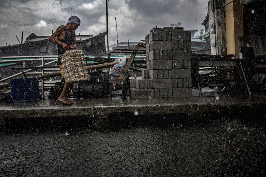 A porter carries eggs from a boat to the market during a downpour.  Everything has to be shipped into Binuangan Island from the main island of Luzon. Credit: James Whitlow Delano