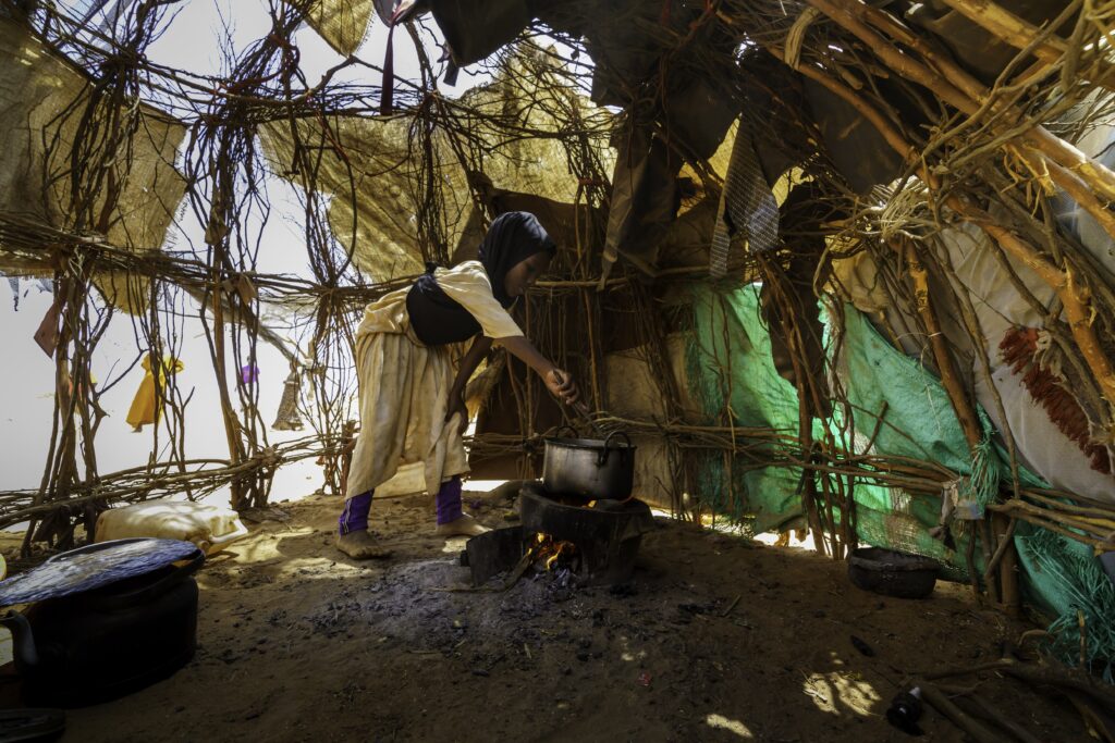 A small girl cooks inside a halfway completed hut at a refugee arrival area near Dadaab, Kenya. Credit: Larry Price