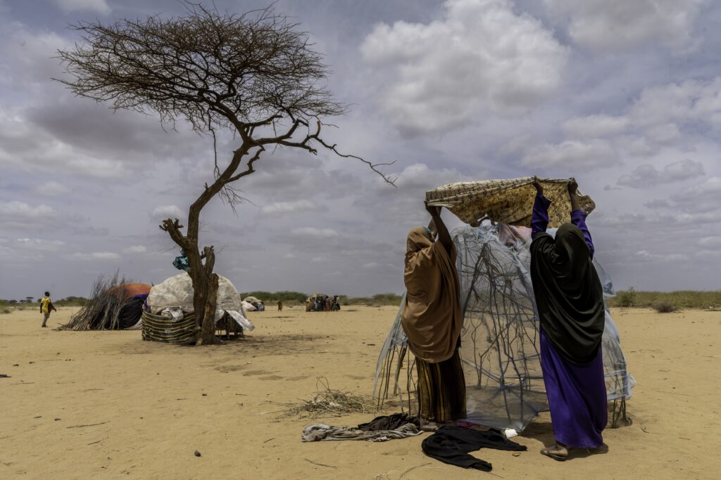 Two women, who just arrived from nearby Somalia, lift pieces of cloth to cover a crude framework of sticks that will be their new home. Credit: Larry Price