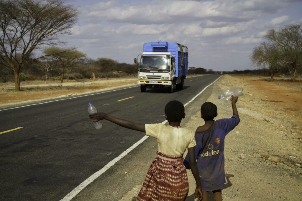 Children stand beside the road to Dadaab, attempting to flag passing cars hoping for handouts of clean bottled water. Credit: Larry Price